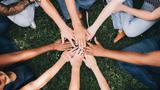 People stacking hands together in the park, photo by Rawpixel/Getty Images