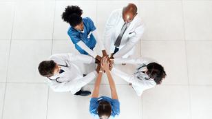 Health care staff stacking their hands together in a hospital, photo by PeopleImages/Getty Images