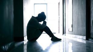 Silhouette of a teenage girl sitting on the floor with her head down, photo by xijian/Getty Images