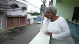 A senior black woman looking out from home balcony looking at neighborhood, photo by Marco/Adobe Stock