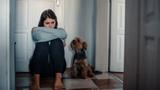 Young white woman looking upset sitting on the floor indoors with a dog next to her, photo by ArtistGNDphotography/Getty Images