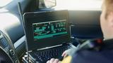 Male police officer using his laptop while out on patrol, photo by PeopleImages/Getty Images