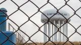 Water tower of Flint Michigan through a chain linked fence, photo by ehrlif/Getty Images