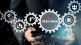 Gear wheels with icons representing aspects of resiliency and the word "Resilience" on them, superimposed over hands holding a tablet, image by Parradee/Adobe Stock.