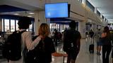 Travelers walk past a monitor displaying a blue error screen at Newark International Airport in Newark, New Jersey, July 19, 2024, photo by Bing Guan/Reuters