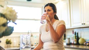Woman standing at kitchen counter drinking water from a glass, photo by eyecrave productions/Getty Images
