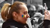 A woman with a blue and yellow heart on her face, showing support for Ukraine, records video on her phone, photo by JANIFEST/Depositphotos