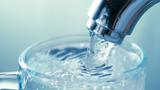 A clear glass cup under a water faucet with water flowing, photo by by sonmez/Getty Images