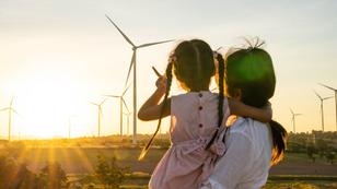 Mother and child in front of wind turbines and a setting sun, photo by Getty Images