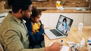 A black man holding a child on his knee conducts a telemedicine appointment with a medical professional via a laption. Photo by Drazen Zigic / Getty Images