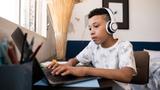 A boy using a laptop and wearing headphones in his room, photo by Vergani_Fotografia/Getty Images