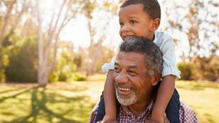 A smiling older man with a young boy sitting on his shoulders