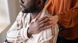 A man in a wheelchair covering his caregiver's hand on his shoulder while looking out a window, photo by pressmaster/Adobe Stock