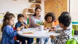 Group of young children coloring with their teacher, photo by Hispanolistic/Getty Images