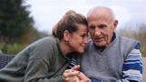 Older father and adult daughter sitting side by side in the garden, photo by Leylaynr/Getty Images