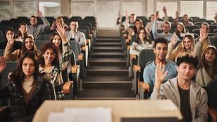 College classroom with students, many raising hands, photo by skynesher/Getty Images