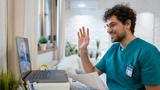 Male nurse waving to a person on a laptop screen, photo by FluxFactory/Getty Images