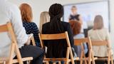 Group meeting seen from the back, participants sitting in wooden chairs, photo by jeffbergen/Getty Images