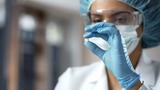 Closeup of a Black woman chemist wearing PPE looking at a white pill, photo by Motortion/Getty Images