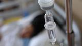 Closeup of an IV drip with a patient in a hospital bed blurred in the background, photo by sutichak/Adobe Stock 