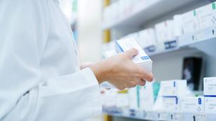 Close up of a pharmacists holding a box of prescription medication in front of shelves stocked with prescription medication, photo by Jacob Wackerhausen/Getty Images