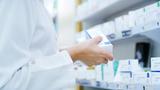 Close up of a pharmacists holding a box of prescription medication in front of shelves stocked with prescription medication, photo by Jacob Wackerhausen/Getty Images