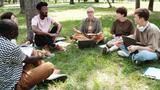 A group of students sitting on the grass and listening to their teacher outdoors, photo by AnnaStills/Adobe Stock
