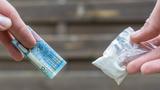 Close up of two hands in an exchange, one holding money and the other holding a small bag of white powder, photo by Ralf Geithe/Getty Images