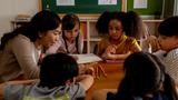 Teacher and young students sitting around a table looking at a pile of pencils, photo by twinsterphoto/Adobe Stock