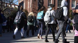 Students wearing backpacks seen from behind as they walk towards a school building. Photo by Sharkshock / Adobe Stock