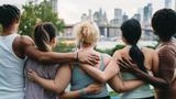 A multiethnic group of young people with arms around each other's shoulders looking out at New York City, photo by FilippoBacci/Getty Images