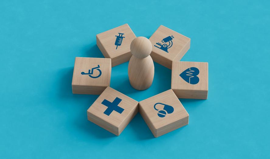 Wood blocks with health care and public health icons surrounding a wood peg figure, photo by MotionIsland/Getty Images
