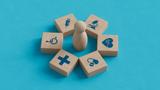 Wood blocks with health care and public health icons surrounding a wood peg figure, photo by MotionIsland/Getty Images