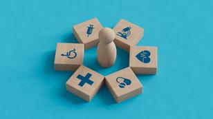 Wood blocks with health care and public health icons surrounding a wood peg figure, photo by MotionIsland/Getty Images