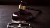 A gavel and handcuffs in a courtroom, photo by vladans/Getty Images
