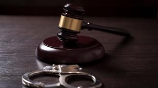 A gavel and handcuffs in a courtroom, photo by vladans/Getty Images