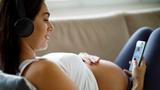 Young pregnant woman reclining and looking at her phone, photo by damircudic/Getty Images