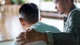 Seen from behind, a young man putting his arm around his friend, photo by AsiaVision/Getty Images