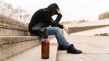 Beer bottle in the foreground, young person with hood pulled over his head sitting on a step in the background, photo by Dani DG/Getty Images