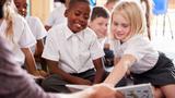 Male teacher reading to a group of elementary school students in uniforms, photo by Adobe Stock