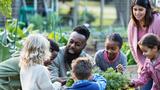 A man teaching a group of children how to grow vegetable plants in a garden, photo by kali9/Getty Images