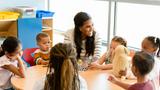 A happy female teacher at a table with preschool-aged children, photo by SDI Productions/Getty Images 