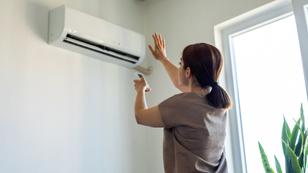 Woman turning on air conditioner, photo by bymuratdeniz/Getty Images