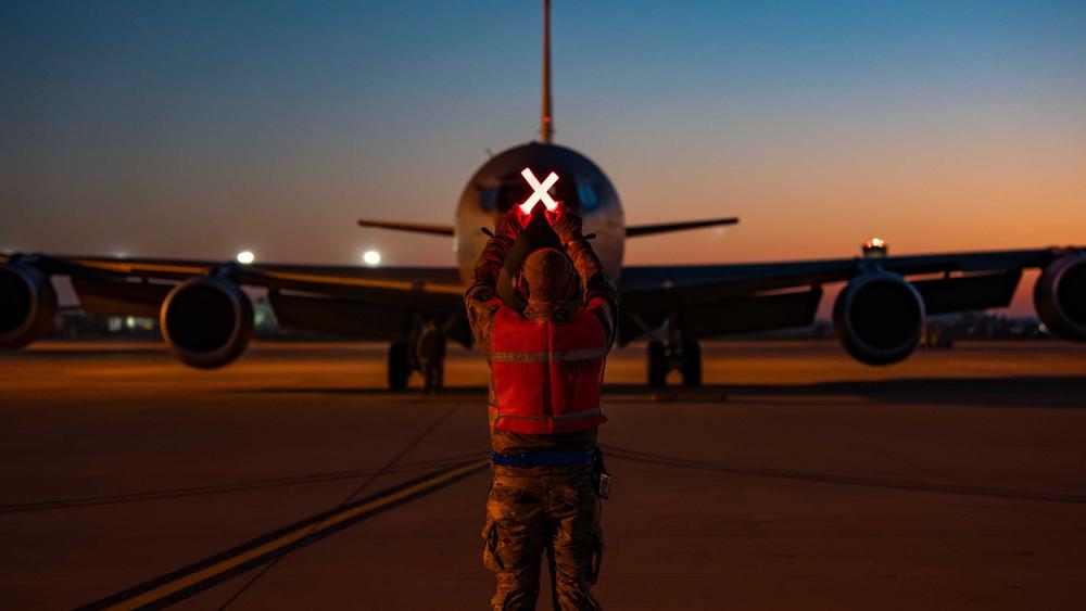 military plane being directed on runway by man with aircraft marshalling wands