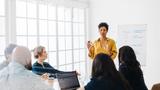 Woman giving a presentation to a group of professionals, photo by Julia Amaral/Adobe Stock.