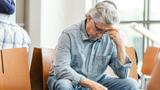 Older man sitting in a waiting room, holding his head in his hand and looking at the floor, photo by SDI Productions/Getty Images