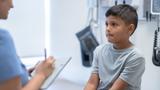Nurse holding a clipboard and talking to a young boy sitting in a doctor's office, photo by FatCamera/Getty Images
