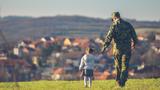 Young girl holding the hand of a man in military fatigues, walking in a field with a city in the background, photo by Photographer and Illustrator/Getty Images