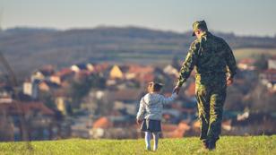 Young girl holding the hand of a man in military fatigues, walking in a field with a city in the background, photo by Photographer and Illustrator/Getty Images