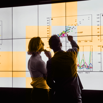 Two researchers analyzing data on a video wall